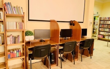 Trzy biurka z komputerami, nad nimi na ścianie biały ekran