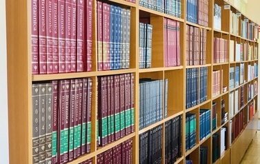 Zbliżenie na regały wypełnione encyklopediami w czerwonych, zielonych i granatowych okładkach