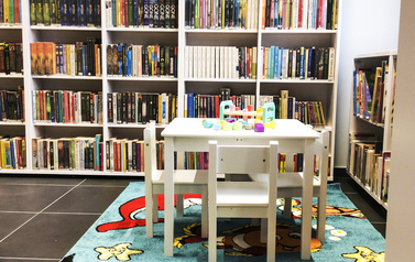 Biały stolik z krzesełkami dla dzieci na kolorowym dywanie, w tle białe regały z książkami
