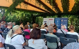 Widownia zebrana na spotkaniu autorskim w parku miejskim.