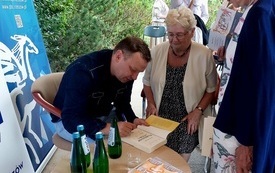 Mężczyzna podpisuje książki czytelnikom.