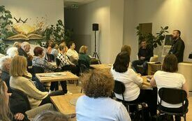 Grupa ludzi siedzi, autor Michał Śmielak stoi i opowiada.