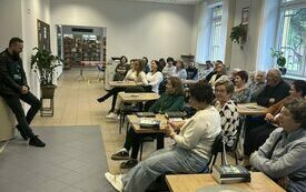 Grupa ludzi siedzi, przed nimi stoi autor Michał Śmielak. 