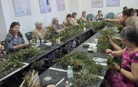 Stół z ziołami i kwiatami, wokół którego siedzą kobiety.