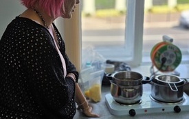 Kobieta w różowych włosach stoi przy przenośnej kuchence.