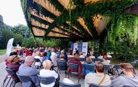 Wiele osób siedzących na krzesłach w parku.