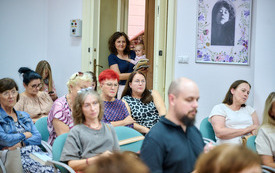 Widok na siedzącą publiczność, w drzwiach kobieta z dzieckiem na ręku.