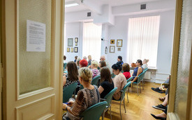 Widok zza uchylonych drzwi na publiczność zgromadzoną w sali