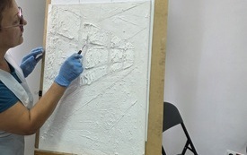 Na sztaludze podobrazie z nieniesioną gładzią. Obok kobieta nanosząca poprawki.