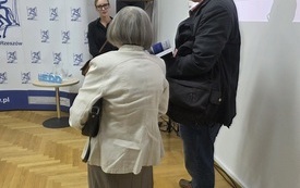 Starsza kobieta i mężczyzna rozmawia z prowadzącą spotkanie kobietą. 