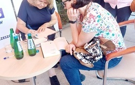 Dwie kobiety przy stoliku, jedna z nich podpisuje książkę.