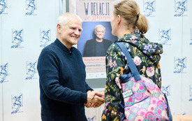 Profesor wymienia uścisk dłoni z kobietą uczestniczącą w spotkaniu. 