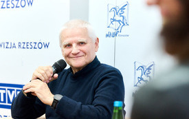 Mężczyzna siwowłosy z mikrofonem w ręku. 