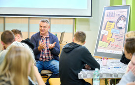 Prowadzący spotkanie mężczyzna mówi do zebranej młodzieży.