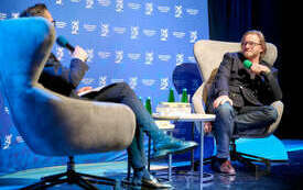 Kadr przedstawiający pisarza siedzącego z mikrofonem na fotelu. 