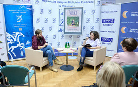 Dwa fotele, gość i prowadząca spotkanie, w tle ścianki z logotypami. 