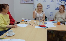 Kobieta w okularach i jasnych włosach trzyma w ręku zdjęcie portretowe starszego mężczyzny.