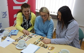 Trzy kobiety przeglądają leżące na stole zdjęcia r&oacute;żnych os&oacute;b.