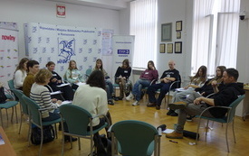 Wok&oacute;ł sali na krzesełkach siedzą uczestnicy warsztat&oacute;w.