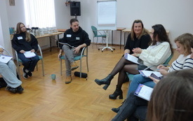 Prowadzący warsztaty zwr&oacute;cony w kierunku kobiety w białym swetrze.