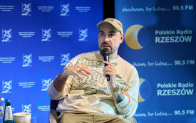 Mężczyzna w czapce z daszkiem z mikrofonem, w tle baner Biblioteki i Radia Rzesz&oacute;w