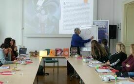 Prowadząca spotkanie pisze na tablicy. Obok uczestnicy spotkania.