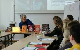 Grupa kobiet siedząca przy stole. Na stole książki, notatniki, kleje biurowe.