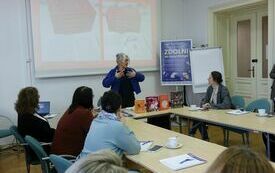 Kobieta w kobaltowej narzutce przemawia do uczestniczek zebranych na warsztatach