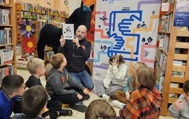 Mężczyzna prowadzący warsztaty w bibliotece i dzieci uczestniczące w nich. 