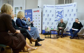 Autor i prowadzący siedzą przed salą pełną czytelnik&oacute;w