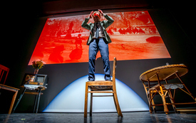 Meżczyzna stoi na krześle będącym częścią scenografii teatralnej