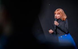 Kobieta z mikrofonem patrzy w kierunku ekranu multimedialnego