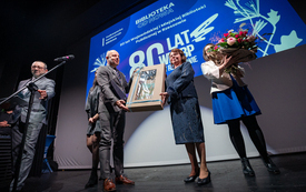 Mężczyzna i kobieta stoją na scenie trzymając razem prezent