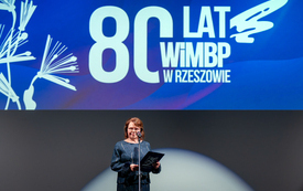 Kobieta przemawiająca ze sceny, nad nią napis 80 lat WiMBP w Rzeszowie