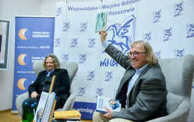 Dw&oacute;ch starszych mężczyzn siedzi w fotelach, w tle banery.