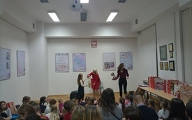 Kobieta w czerwonej sukience wręcza prezent dziewczynce z długimi włosami.