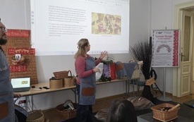 Kobieta i mężczyzna w fartuchu, za nimi na stole materiały do warsztat&oacute;w