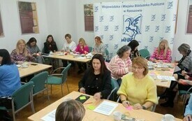 Przy stolikach siedzą uczestnicy spotkania. W tle banner z pegazem.