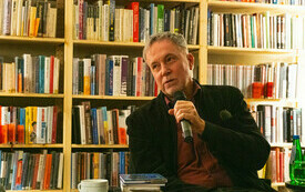 Meżczyzna z mikrofonem, za nim widoczny regał pełen książek