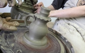 Koło garcarskie i dwie pary rąk kształtujące gliniany dzbanek