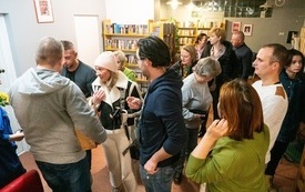 Grupa czytelnik&oacute;w stoi między bibliotecznymi p&oacute;łkami