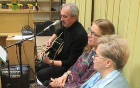 Mężczyzna gra na gitarze, obok niego siedzą dwie kobiety. 