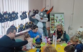 Grupa os&oacute;b dorosłych i dzieci siedzi przy stole i wykonuje ozdoby wielkanocne
