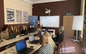 Gruopa starszych os&oacute;b siedzących przed laptopami ogląda prezentację na temat zakup&oacute;w w internecie
