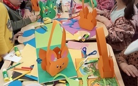 St&oacute;ł z materiałami plastycznymi potrzebnymi do wykonania koszyczk&oacute;w. Na stole kolorowe papiery, flamastry i gotowe kosztczki.