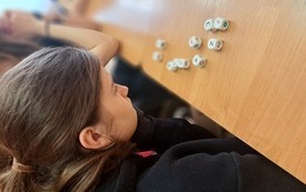 Nastolatka w kucyku patrząca na rozsypane na stoliku kostki do gry na ściankach, kt&oacute;rych znajdują się litery. 