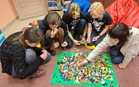 Pięć młodych os&oacute;b układających klocki Lego.