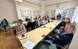 Uczestnicy konferencji siedzący przy stolikach. w tle wystawa oraz baner z pegazem. 