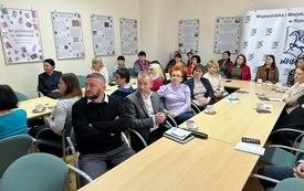 Uczestnicy konferencji kobiety i mężczyźni siedzący przy stolikach. 