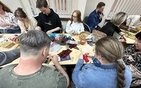 Uczestnicy warsztat&oacute;w wykonują szmaciane lalki z kawałk&oacute;w materiału, wł&oacute;czek, orzech&oacute;w i ziarna. 